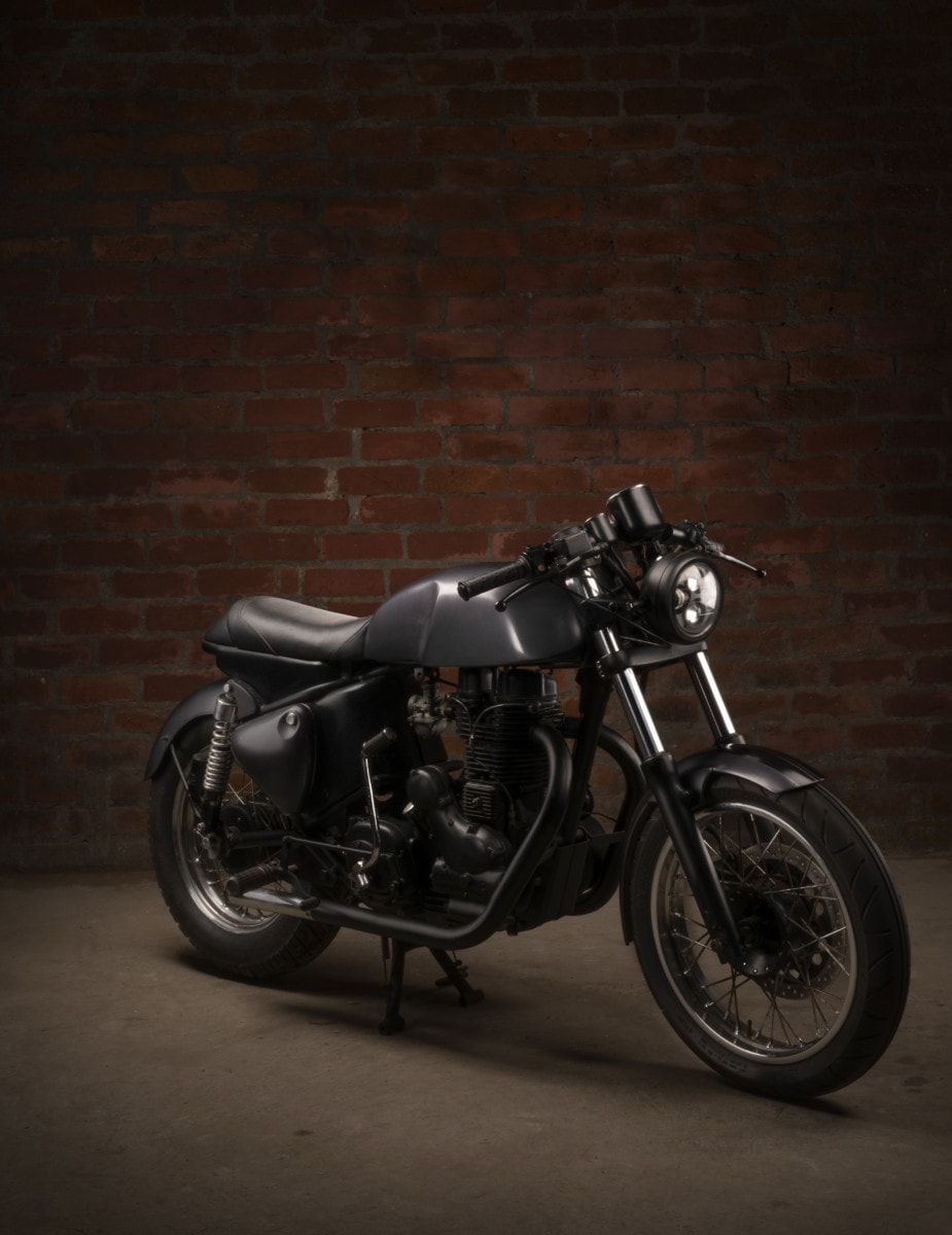 Black 1975 Royal Enfield Bullet 350 cafe racer in a dark studio with a brick wall