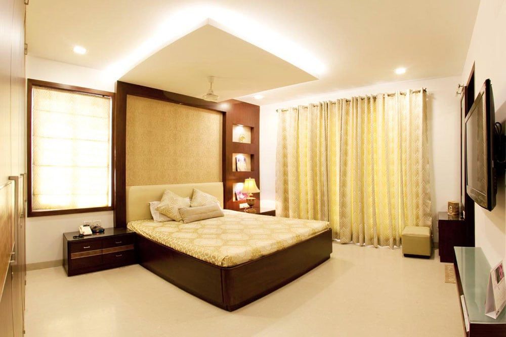 Bedroom with a backlit panelled headboard, gold curtains and a cove-lit ceiling