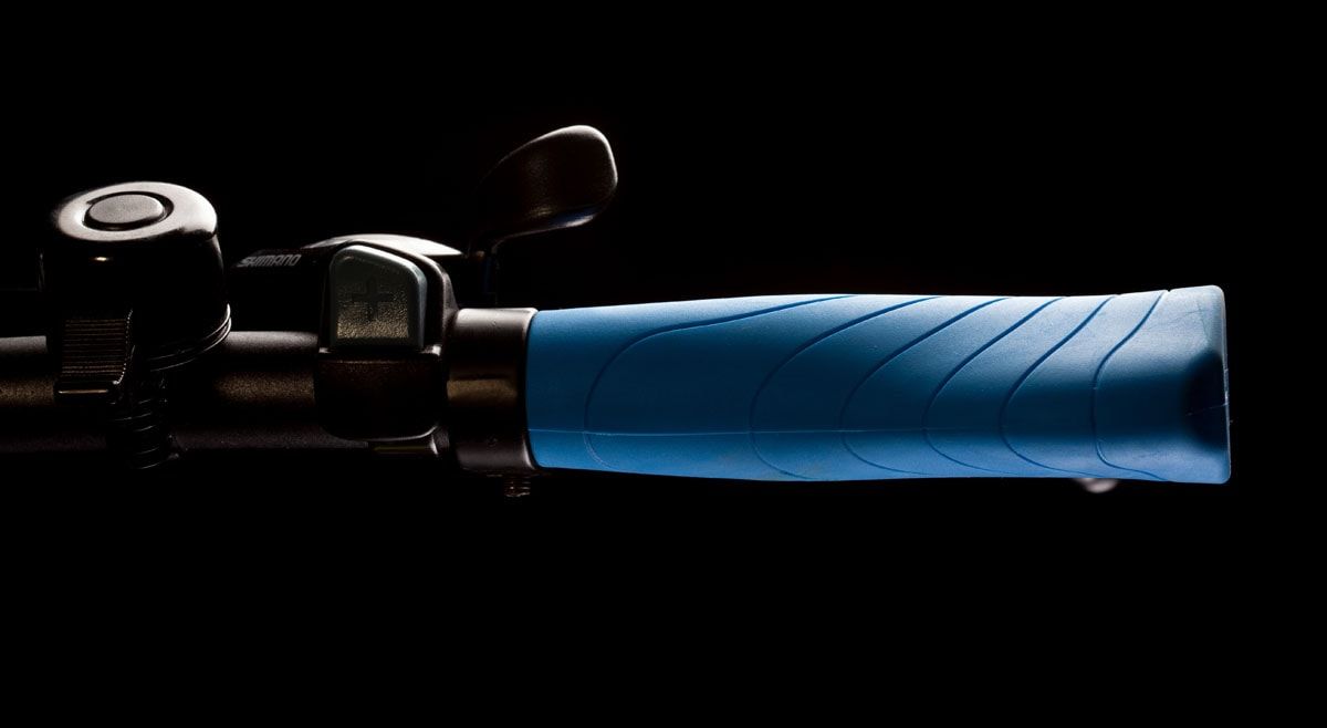Blue bicycle grip with a bell and brake lever on the handlebar, against black