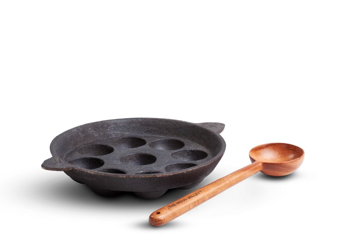 Cast iron paniyaram pan with a wooden ladle, on a white background