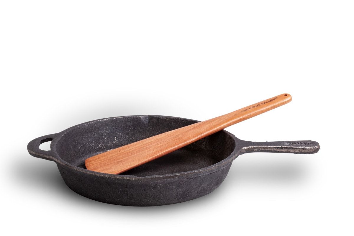 Cast iron skillet with a wooden spatula resting across it, on a white background