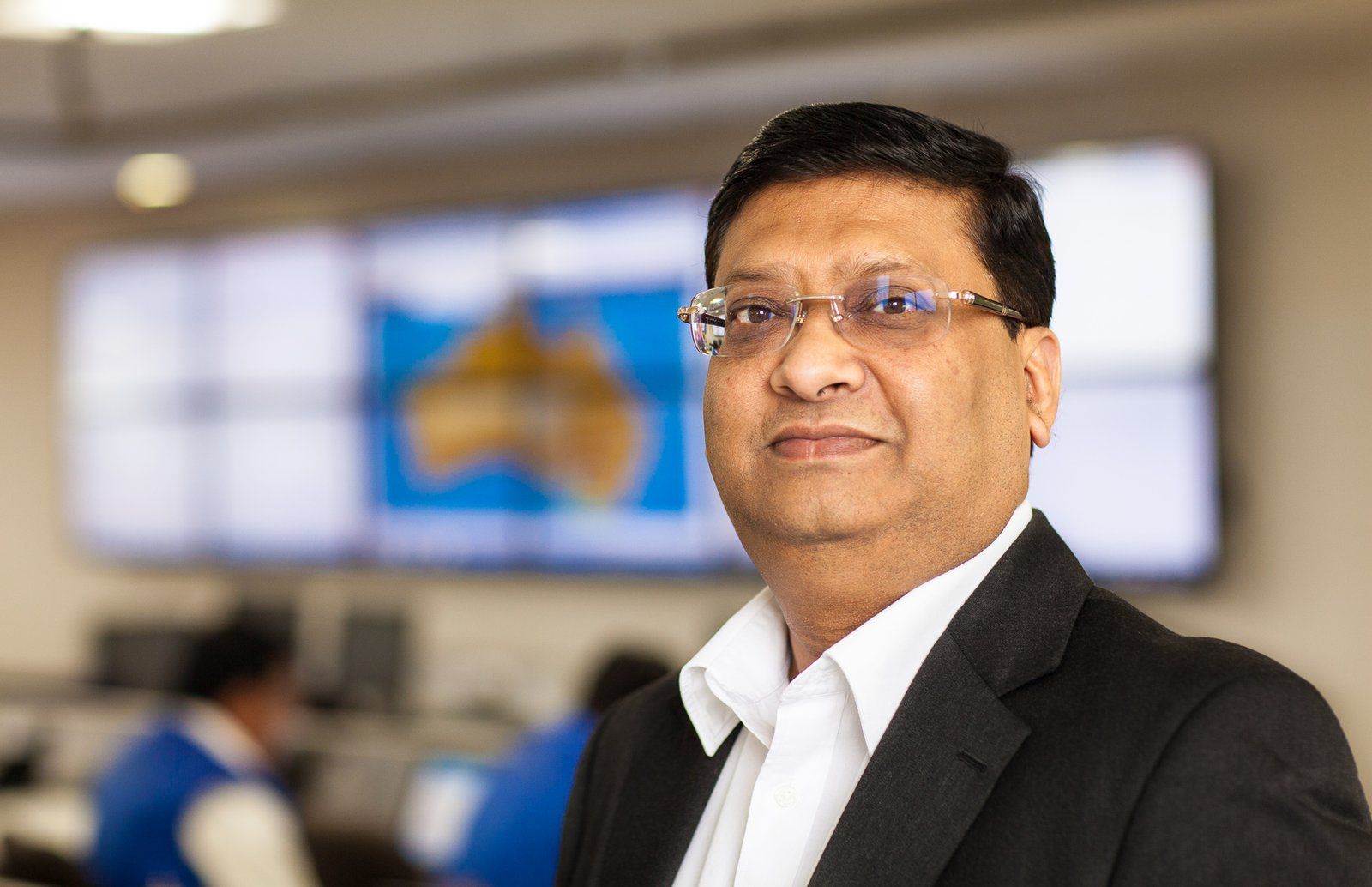 Smiling executive in a dark suit in front of a control room video wall