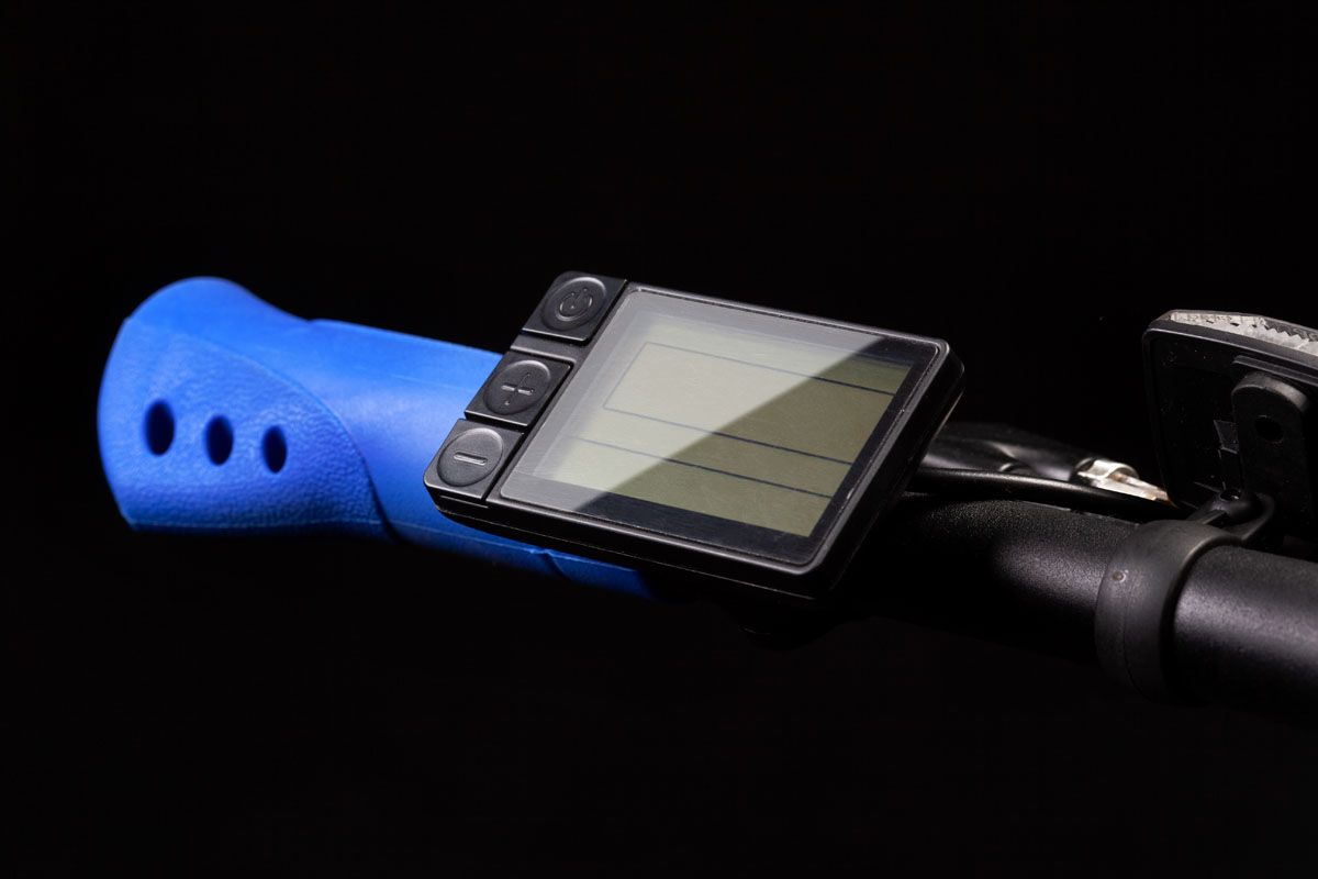 Electric bicycle handlebar display beside a blue grip, against black