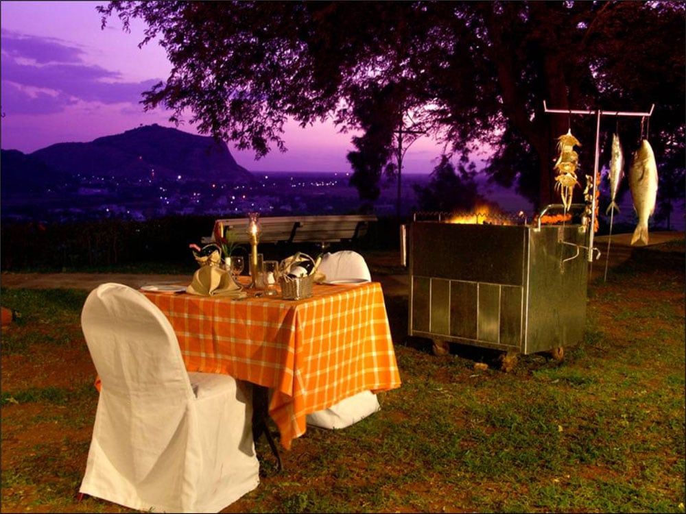 Candlelit table and barbecue set up on a hilltop at dusk, town lights below