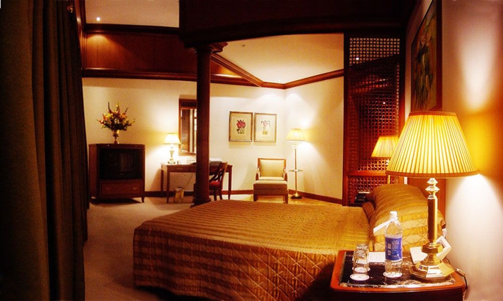 Hotel room in warm lamplight with a quilted bed, armchair and wooden screens