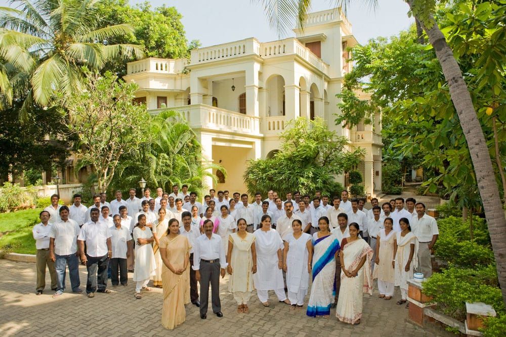 Hotel staff in uniform gathered for a group portrait in front of a white colonial building