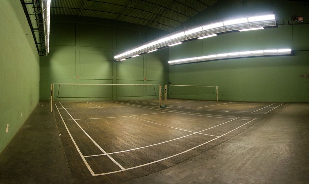 Indoor badminton court with green walls and a wooden floor under strip lights