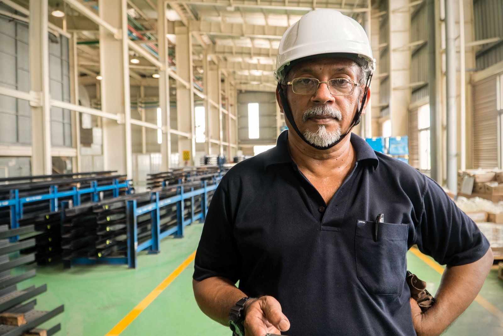 Man in a white hard hat, hands on hips, on a factory floor