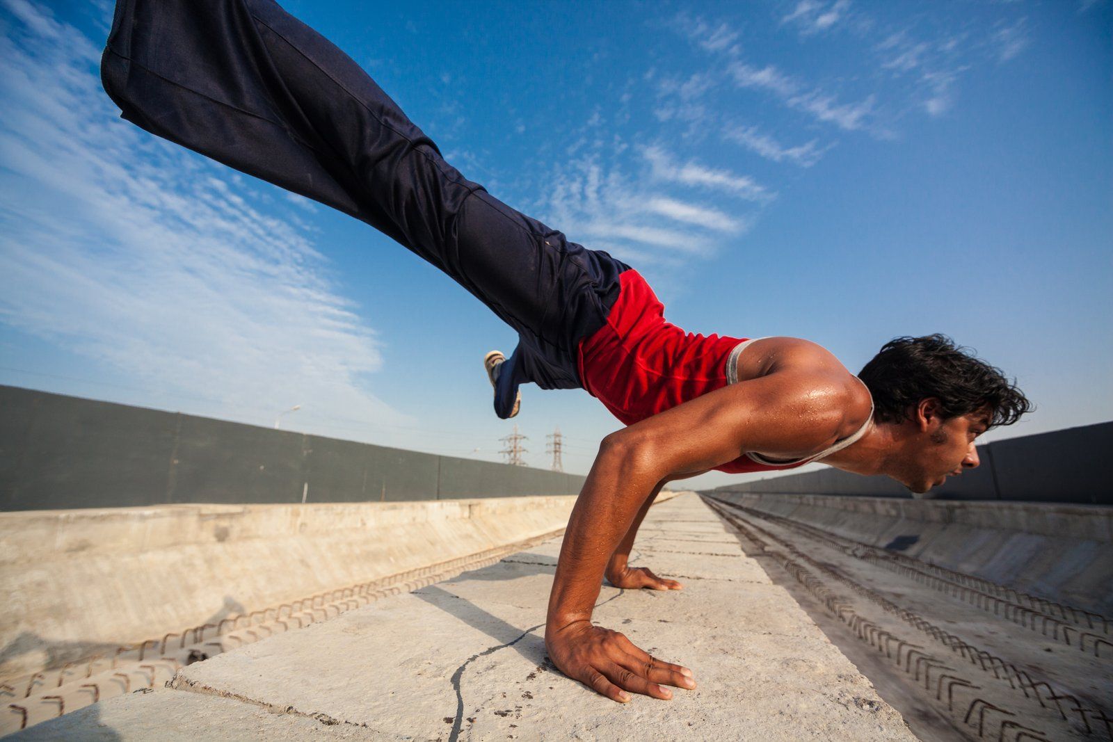 Parkour athlete holding a one-arm balance on a rooftop ledge under a blue sky