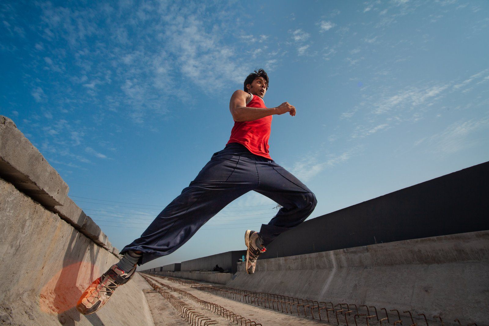 Parkour athlete leaping between rooftop ledges against a blue sky
