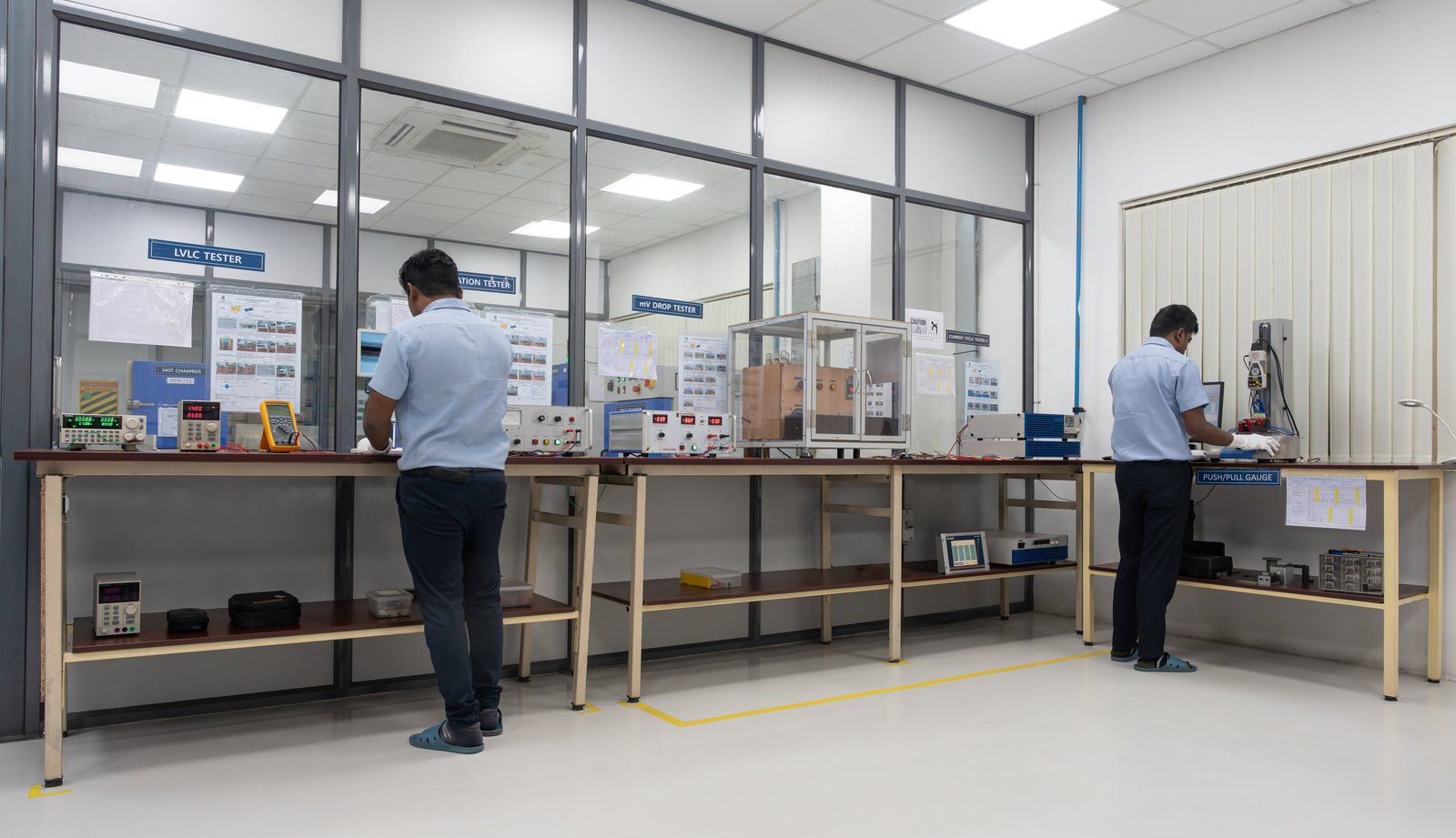 Technicians at work benches in a glass-walled quality testing lab at Besmak