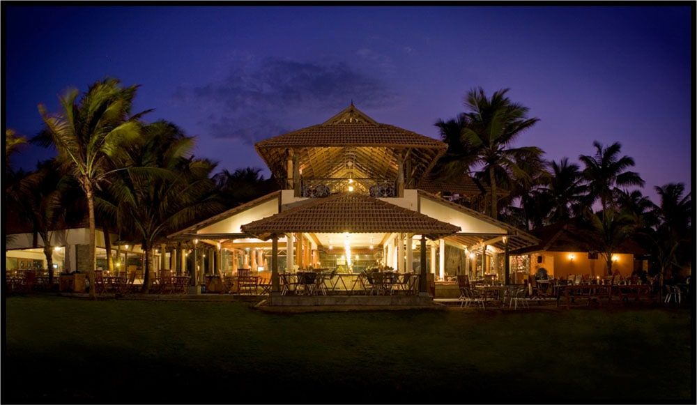 Tiled-roof restaurant pavilion glowing at night among coconut palms