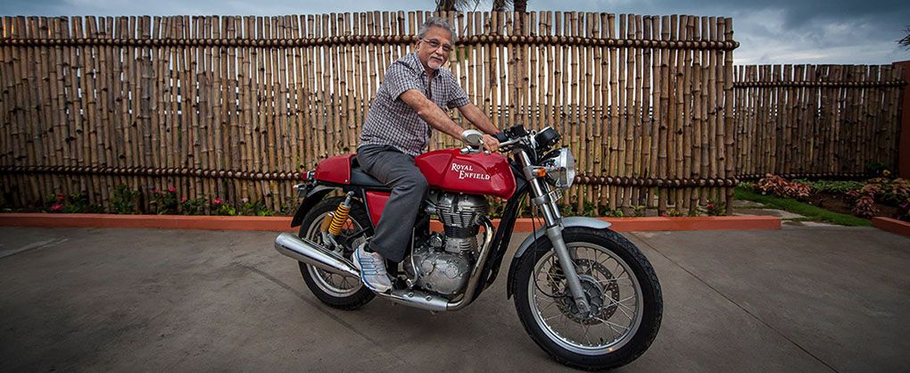 R. L. Ravichandran seated on a red Royal Enfield Continental GT in front of a bamboo fence