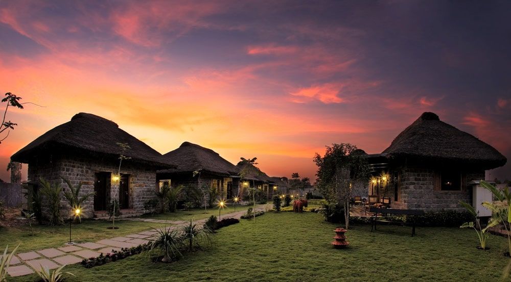 Thatched stone cottages on a resort lawn under a red sunset sky