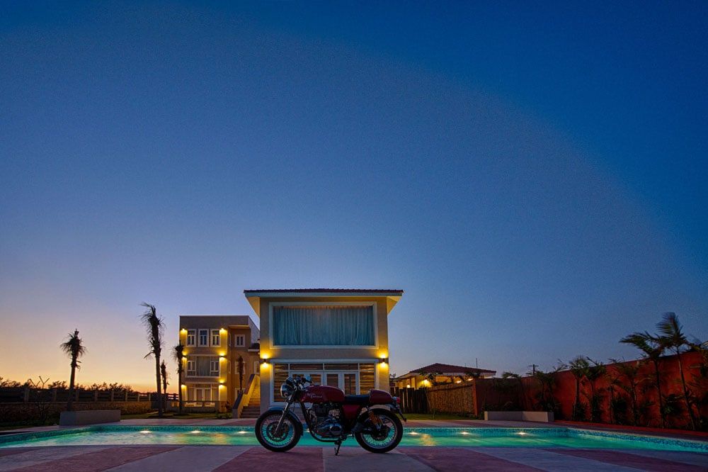 Two-storey villa lit at dusk beside a pool, with a motorcycle parked at the edge