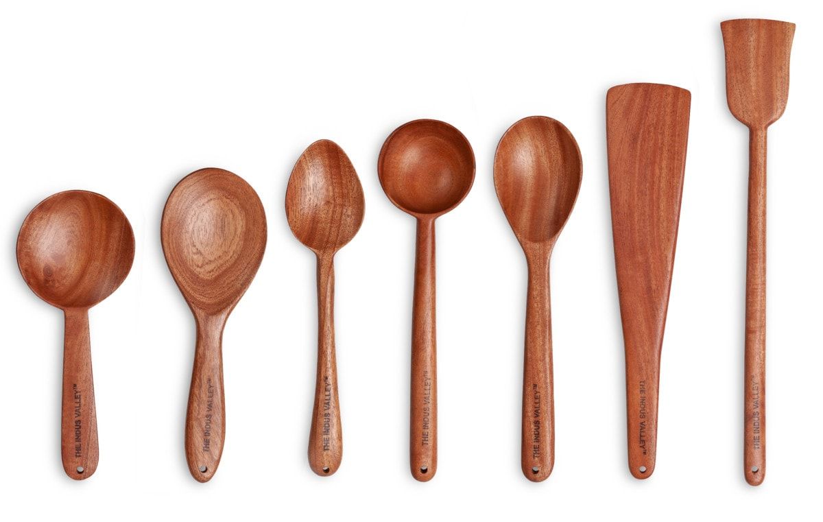 Seven wooden ladles and spatulas standing in a row on a white background
